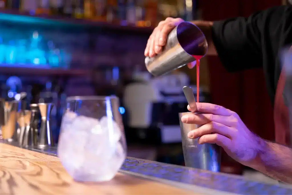 Bartender pouring red cocktail into shaker.